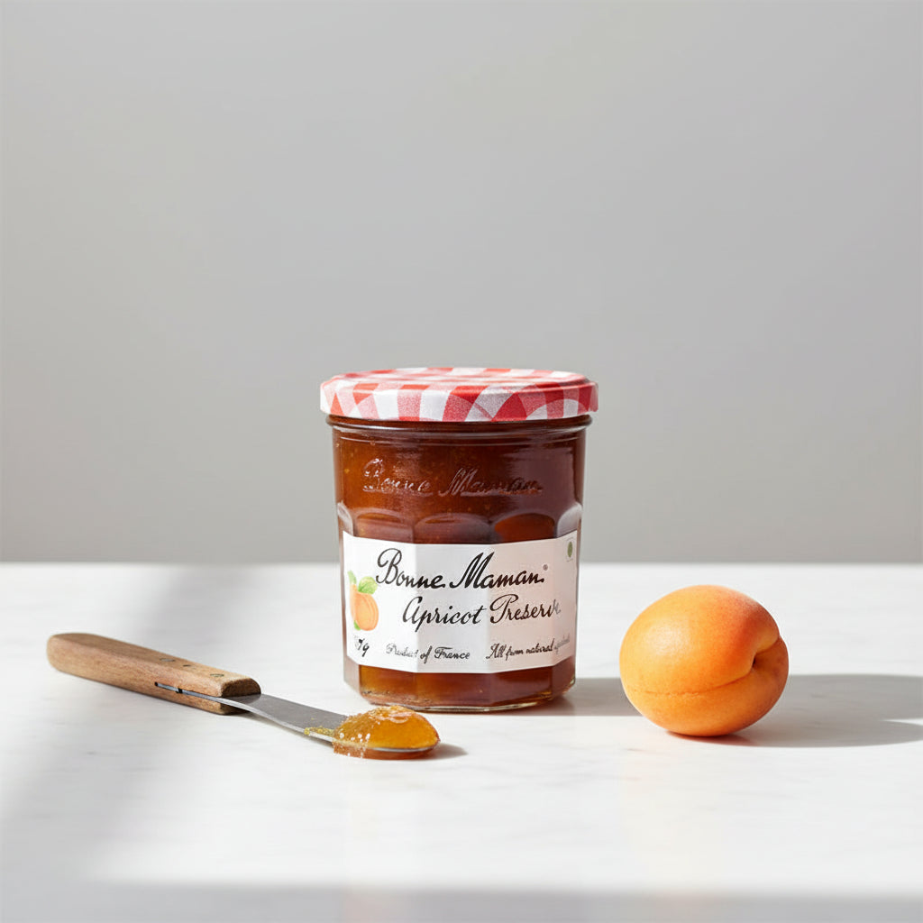 A glass jar of Bonne Maman Apricot Preserves with a red and white checkered lid, set against a plain white background.