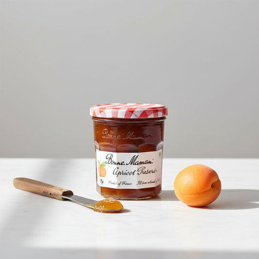 A glass jar of Bonne Maman Apricot Preserves with a red and white checkered lid, set against a plain white background.