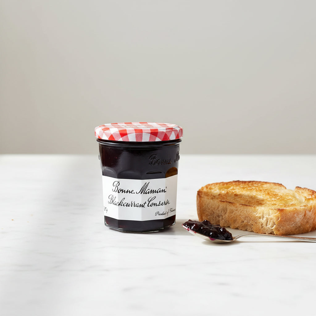 A glass jar of Bonne Maman Blackcurrant Conserve with a red and white checkered lid and a white label, shown against a plain off-white background.