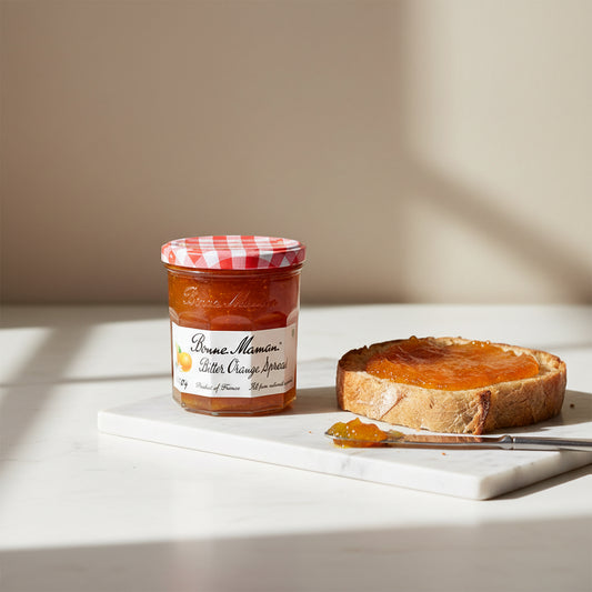 A glass jar of Bonne Maman Butter Orange Spread with a red and white checkered lid, set against a plain off-white background.
