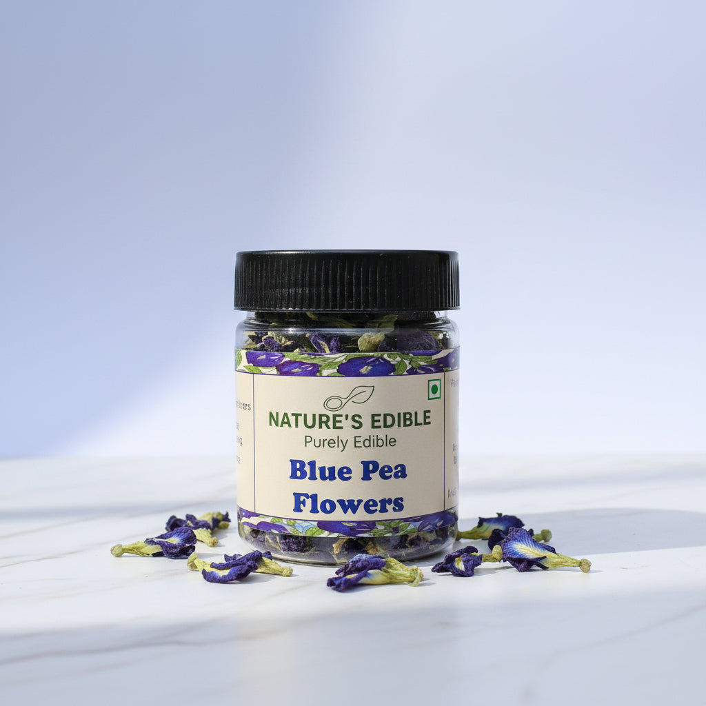 A jar of Nature's Edible Blue Pea Flowers, featuring a black lid and a cream-colored label with purple and green accents, set against a textured pinkish-beige background.